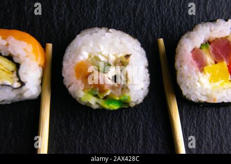 Les bâtonnets contiennent des rouleaux qui se tiennent sur un plateau en graphite noir pour les sushis qui se tiennent sur un fond noir et un rouleau pour un tour de sushi Banque D'Images