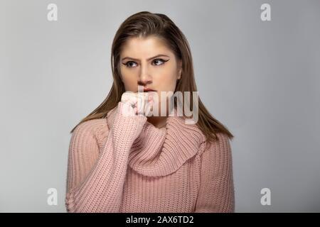 Gros plan portrait d'une jeune femme caucasienne portant un pull rose sur fond gris. Elle a l'air en colère et en stress Banque D'Images