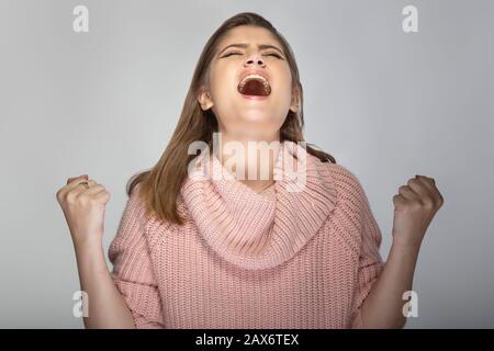 Gros plan portrait d'une jeune femme caucasienne portant un pull rose sur fond gris. Elle a l'air en colère et en stress Banque D'Images