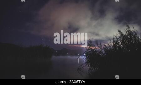 Photo nocturne d'un lac avec lumière réfléchissant sur le distance et teintes roses dans le ciel Banque D'Images