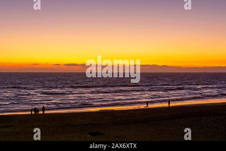 Coucher de soleil sur l'Océan Pacifique avec silhouettes de personnes sur la plage à Huntington Beach, Californie. Banque D'Images