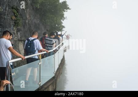 Zhangjiajie, Chine - Août 2019 : Les Touristes marchant sur une allée étroite en verre dans le parc naturel de Tianmenshan Banque D'Images
