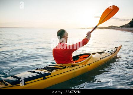 Vue arrière de l'homme plus âgé, faites du kayak sur la mer au coucher du soleil Banque D'Images