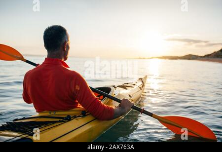 Vue arrière de l'homme plus âgé, faites du kayak sur la mer au coucher du soleil Banque D'Images