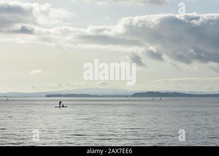 Paddle-board à distance sur la surface du grand port très calme à l'arrière-plan. Banque D'Images