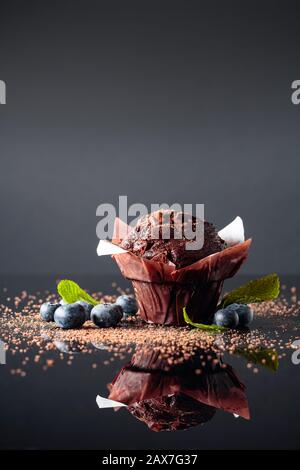 Muffin au chocolat saupoudré de miettes de chocolat noir sur un fond réfléchissant. Aux fruits rouges muffins et de menthe. Copier l'espace. Banque D'Images