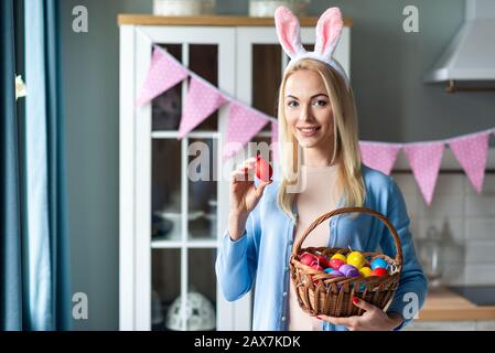 Portrait d'une jolie femme portant des œufs de lapin et debout. Elle possède un panier avec des œufs de Pâques colorés et en montre un Banque D'Images