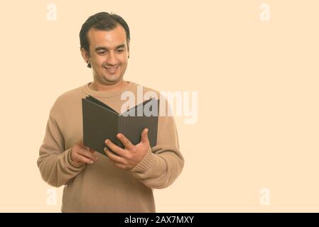 Studio shot of Persian man smiling and reading book Banque D'Images