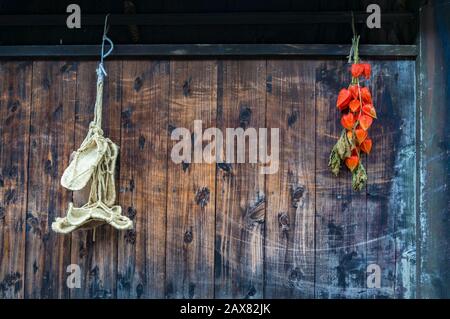 Beau mur en bois avec des dosettes de physalis lumineuses et des sandales japonaises traditionnelles à paille. Arrière-plan artisanal japonais Banque D'Images