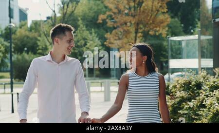 Les couples multiethniques se regardent en se promenant dans la rue, en tenant les mains et en parlant. Concept de relation. Banque D'Images
