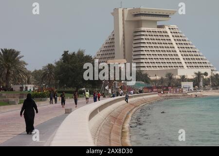 Une femme marche le long de la Corniche à Doha avec l'hôtel Sheraton en vue. Banque D'Images