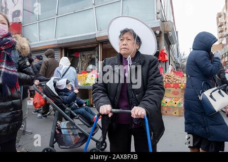 Lors d'un voyage d'achat de nourriture, une ancienne femme chinoise américaine dans un grand chapeau attend de traverser Main St. dans Chinatown, Flushing, Queens, New York City. Banque D'Images