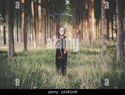 Jeune femme avec scythe et masque dans la forêt Banque D'Images