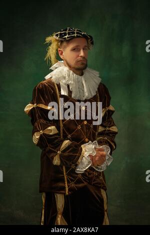 Se poser pensive. Portrait du jeune homme médiéval dans des vêtements vintage debout sur fond sombre. Modèle masculin en duke, prince, personne royale. Concept de comparaison des époques, moderne, de la mode. Banque D'Images