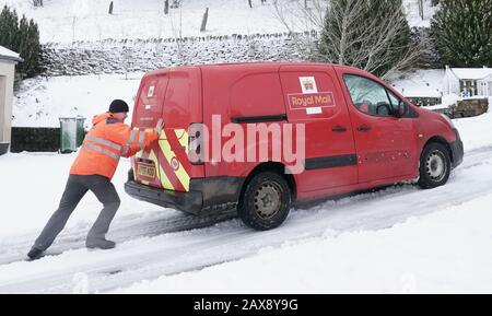 Un travailleur du Royal Mail tente de pousser une camionnette de livraison bloquée sur une route enneigée à Nenthead, Cumbria. Banque D'Images