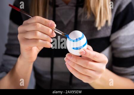 Fille peignant des œufs de Pâques avec un pinceau à une table. La femme décorera l'oeuf avec des motifs bleus. Concept de vacances de Pâques. Gros plan Banque D'Images