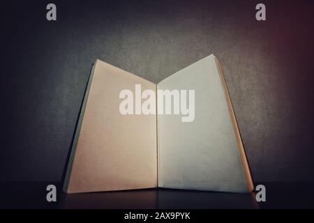 Fermez un livre ouvert, sur la table, avec des pages blanches vierges. Ancien manuel ou bloc-notes avec feuilles vides, espace de copie. Vieux journal isolé sur ba gris foncé Banque D'Images