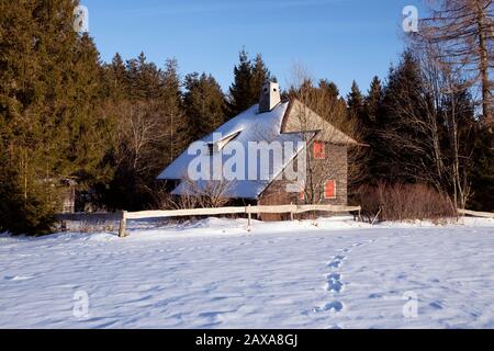 Ancienne maison rurale en bois avec toit enneigé sur le bord de la forêt, empreintes dans la neige, jour ensoleillé d'hiver. Paysage d'hiver, conifères et hu traditionnel Banque D'Images