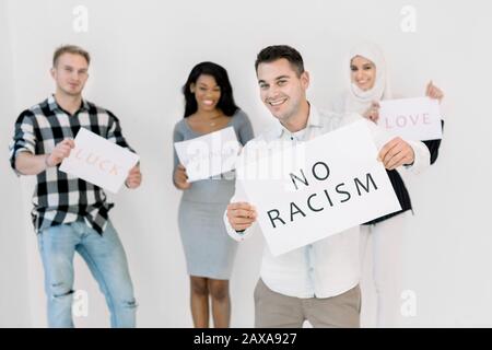 Un homme blanc en tenue décontractée tient une affiche avec le texte sans racisme dans ses mains, debout sur fond blanc. Trois militants multiethniques chantant un Banque D'Images