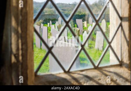 Vue à travers une fenêtre d'église sur le cimetière de l'église, Angleterre, Royaume-Uni Banque D'Images