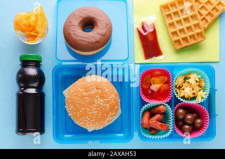 boîte à déjeuner avec nourriture malsaine sur fond bleu, vue de dessus Banque D'Images