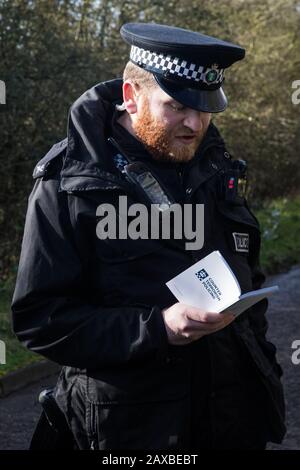 Denham, Royaume-Uni. 11 Février 2020. Un policier de la vallée de la Tamise lit dans un livre intitulé «police contre le terrorisme», puisqu’il émet un avertissement à un militant environnemental de la rébellion de l’extinction, qui avait été «peu marchant» devant un VHG livrant un véhicule élévateur JCB à un site de  . Le militant a par la suite été arrêté. Crédit: Mark Kerrison/Alay Live News Banque D'Images