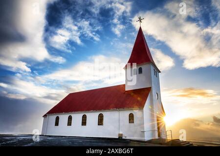 La pittoresque église Vik i Myrdal de Vik, en Islande. Le soleil monte sur la mer derrière, provoquant des flares et une étoile de soleil. Banque D'Images