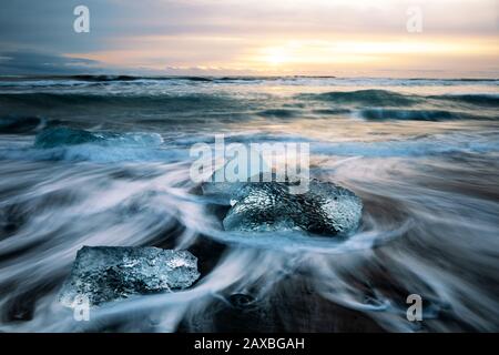 Lever Du Soleil Sur Diamond Beach, Islande. Les sables volcaniques noirs sont jonchés de Canards de glace glaciale qui ont cassé de la lagune presque de glacier an Banque D'Images