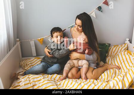 Jeune belle mère avec ses enfants sur le lit, étroitement embrasse son fils et fille, embrasse son front, les enfants rient Banque D'Images