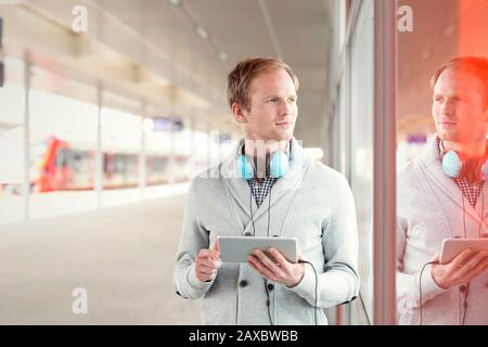 Jeune homme avec tablette numérique et casque en attente près de la plate-forme de la gare Banque D'Images