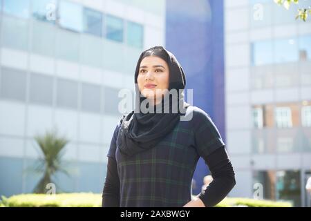 Portrait une jeune femme confiante portant du hijab à l'extérieur du bâtiment ensoleillé Banque D'Images