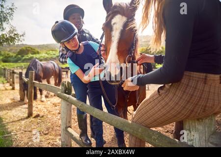 Femme et filles préparant le cheval pour l'équitation à l'équitation paddock Banque D'Images