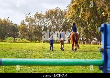 Femme enseignant des filles équitation dans l'herbe rurale ensoleillée paddock Banque D'Images