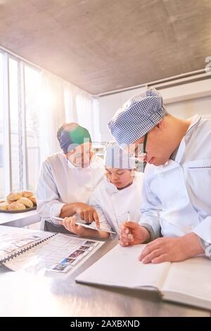 Chef et étudiants avec syndrome De Down utilisant tablette numérique dans la cuisine Banque D'Images