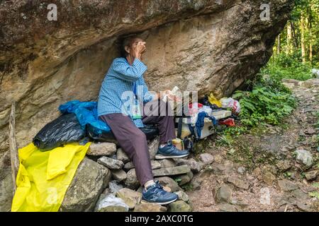 Zhangjiajie, Chine - Août 2019 : Pauvre vieille femme ouvrier reposant sous un énorme rocher rocheux sur un sentier dans le parc national de Zhangjiajie Banque D'Images