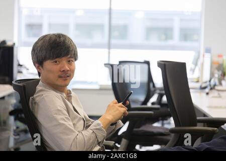 Portrait d'un homme d'affaires confiant avec smartphone au bureau Banque D'Images