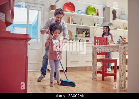 Père et fille balayant le sol de la cuisine avec balai Banque D'Images