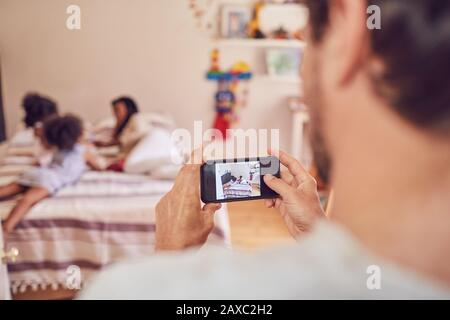 Père avec appareil photo téléphone photographier la famille sur le lit Banque D'Images