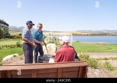 Des amis de golf de sexe masculin parlent de boire de la bière sur le patio ensoleillé du terrain de golf Banque D'Images