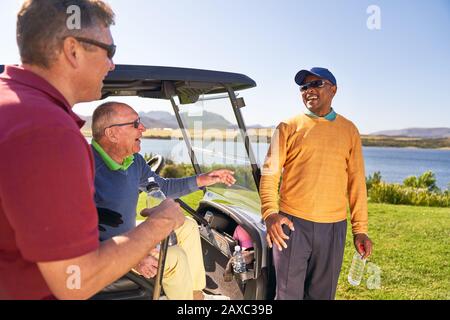 Des amis de golf de sexe masculin parlent et rient sur la voiturette de golf Banque D'Images