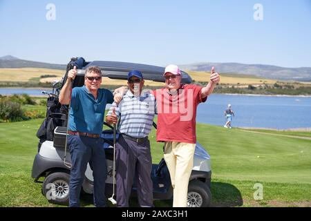 Portrait heureux adultes golfeurs de sexe masculin à la voiturette de golf sur le terrain ensoleillé Banque D'Images