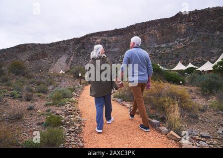 Couple senior tenant les mains sur le sentier à l'extérieur des cabines de pavillon de safari Banque D'Images