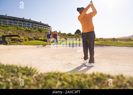 Golfeur masculin prenant un tir hors du bunker ensoleillé Banque D'Images