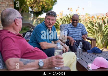 Des amis hommes matures de golf parlent et buvant de l'eau sur le patio Banque D'Images