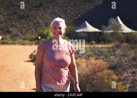 Portrait heureuse femme senior sur sentier ensoleillé à l'extérieur de Safari Lodge Banque D'Images