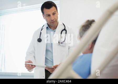 Médecin avec tablette numérique en train de faire des rondes, en parlant avec le patient dans le lit d'hôpital Banque D'Images