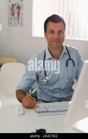 Portrait confiant médecin de sexe masculin travaillant à l'ordinateur dans le bureau des médecins Banque D'Images