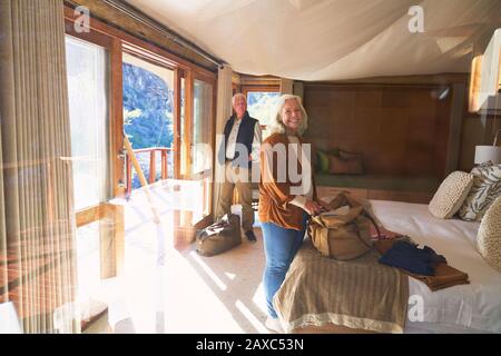 Portrait heureux couple senior déballage dans la chambre d'hôtel ensoleillée Banque D'Images