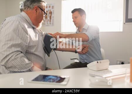 Médecin de sexe masculin vérifiant la tension artérielle du patient principal dans le cabinet de médecins Banque D'Images