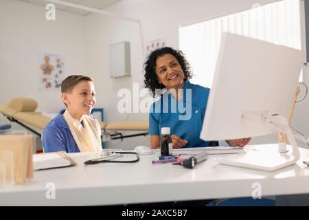 Femme pédiatre et jeune patient parlant, à l'aide d'un ordinateur dans le bureau de médecins Banque D'Images